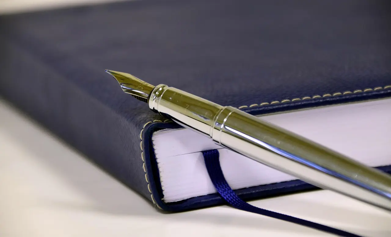 A pen and a closed blank notebook on a plain desk