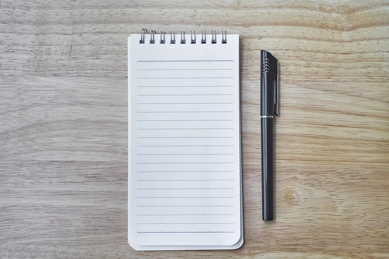 An empty notepad and a pen on a wooden desk